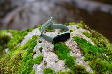 Nehrin kenarında yosunlu bir taş kapağında fitness takip cihazı.