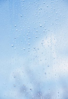 Bokeh arkaplanlı cam yüzeyine yağmur damlaları yağar.