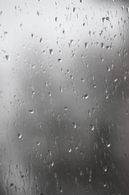 Bokeh arkaplanlı cam yüzeyine yağmur damlaları yağar.