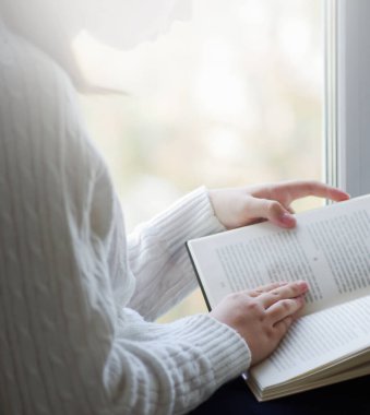 Beyaz yün kazaklı kadın elinde kitap tutarken yakından görülüyor. Kitap konsepti arka planının maketi için boş alan.