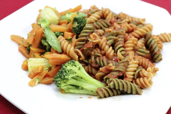 Steamed broccoli, sugar snap peas, carrot, baby corn cob vegetables with tri-color rotini pasta, tomato sauce. A vegetarian meal of a variety of vegetables with tri-color rotini pasta in tomato sauce
