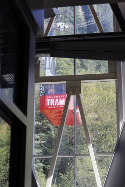 Juneau, AK, ABD - 17 Eylül 2024: Güneşli bir günde, içinde insanların süzülerek kablo yeşil ağaç dağlarında süzüldüğü bir GoldLDBELT TRAM kırmızıya boyandı. Fotoğraf tramvay istasyonunun içinden çekilmiş.