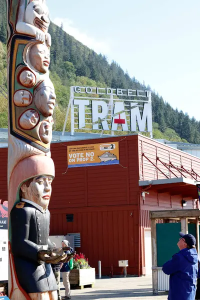 Juneau, AK, ABD - 17 Eylül 2024: Kırmızı bir binanın tepesinde, güneşli bir günde dışarıda bir totem direğinin yanında bir altın sarısı TRAM tabelası. Gündüz bir totemin yanında büyük bir altın sarısı tramvay tabelası.