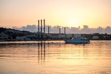 Malta, Marsaxlokk 'ta gündoğumu: sakin bir denizde yatı olan sanayi manzarası