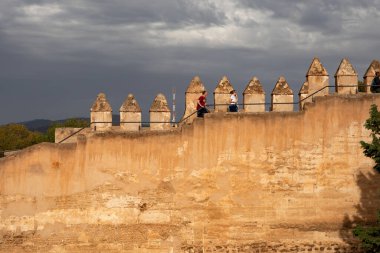 Malaga, Spain - November 17, 2024: The defensive walls of the ancient Gibralfar Castle in Malaga with passers-by against a dramatic sky. clipart