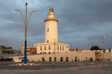 Malaga, Spain - November 17, 2024: Malaga lighthouse La Farola in the evening light with a stormy sky. clipart