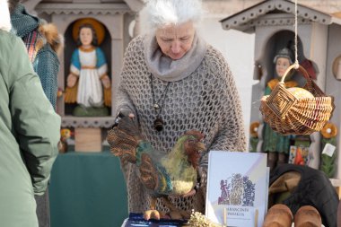Vilnius, Litvanya - 8 Mart 2025: Litvanya 'nın Vilnius kentindeki Kaziukas fuarında el yapımı ahşap horoz ve halk sanatı satan yaşlı zanaatkar.
