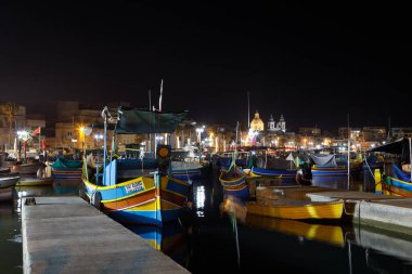 Marsaxlokk, Malta - 11 Ekim 2023: Geceleyin Malta 'nın tarihi Marsaxlokk limanına yanaşan renkli geleneksel luzzu balıkçı tekneleri.
