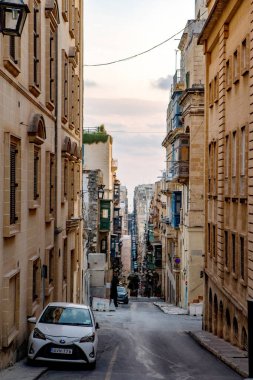 Valletta, Malta - 8 Ekim 2023: Valletta 'da kireçtaşı binalar ve renkli balkonlarla kaplı geleneksel dar bir caddenin manzarası. Görüntü, tarihi Malta başkentinin eşsiz mimari cazibesini ve şehir planlarını yansıtıyor..