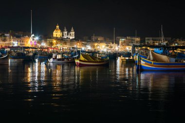 Marsaxlokk, Malta - 11 Ekim 2023: Geceleyin Malta 'nın tarihi Marsaxlokk limanına yanaşan renkli geleneksel luzzu balıkçı tekneleri.