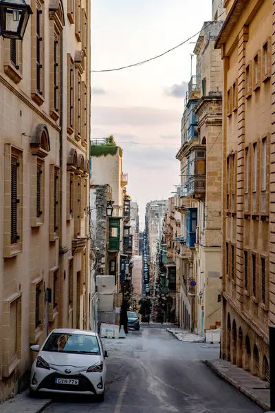 Valletta, Malta - 8 Ekim 2023: Valletta 'da kireçtaşı binalar ve renkli balkonlarla kaplı geleneksel dar bir caddenin manzarası. Görüntü, tarihi Malta başkentinin eşsiz mimari cazibesini ve şehir planlarını yansıtıyor..