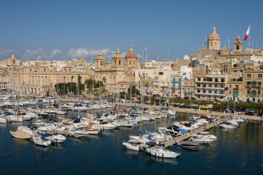 Birgu, Malta - 13 Ekim 2023: Birgu 'daki marinanın panoramik görüntüsü, şehrin tarihi kireçtaşı mimarisi ve önde gelen kubbeleriyle ön planda demirlemiş yelkenli kümesini gösteriyor..