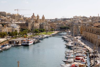 Birgu, Malta - 13 Ekim 2023: Birgu 'daki marinanın panoramik görüntüsü, şehrin tarihi kireçtaşı mimarisi ve önde gelen kubbeleriyle ön planda demirlemiş yelkenli kümesini gösteriyor..