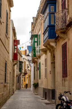 Rabat, Malta - 8 Ekim 2023: Rabat 'ta sakin, dar bir ara sokak, kırmızı, yeşil ve mavi renkli bir dizi parlak boyanmış ahşap balkon içeren geleneksel Malta mimarisini sergiliyor.. 
