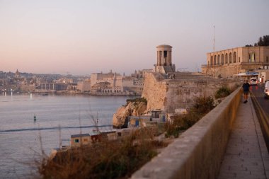 Valletta, Malta - 9 Ekim 2023: Aşağı Barrakka Bahçeleri ve Siege Bell Anıtı, gün doğumunda Grand Harbour 'a tepeden bakar ve Valletta' nın ufuk çizgisi uzaktadır..
