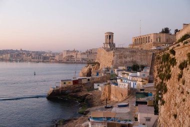 Valletta, Malta - 9 Ekim 2023: Aşağı Barrakka Bahçeleri ve Siege Bell Anıtı, gün doğumunda Grand Harbour 'a tepeden bakar ve Valletta' nın ufuk çizgisi uzaktadır..