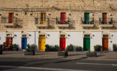 Marsaxlokk, Malta - 11 Ekim 2023: Parlak renkli kapıları ve geleneksel balkonları olan bir dizi bina Marsaxlokk 'ta güneşli bir cadde hizasında..