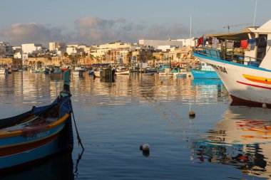 Marsaxlokk, Malta - 13 Ekim 2023: Geleneksel luzzu balıkçı tekneleri Marsaxlokk Limanı 'nı renkli binalarla ve arka planda hareketli bir limanla doldurdu.