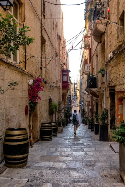 Valletta, Malta - 9 Ekim 2023 Valletta 'da dekoratif fıçılar ve canlı bougainvillea ile süslenmiş dar ve tarihi bir sokakta yalnız bir insan yürüyor..