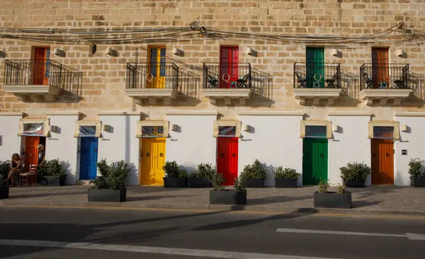 Marsaxlokk, Malta - 11 Ekim 2023: Parlak renkli kapıları ve geleneksel balkonları olan bir dizi bina Marsaxlokk 'ta güneşli bir cadde hizasında..