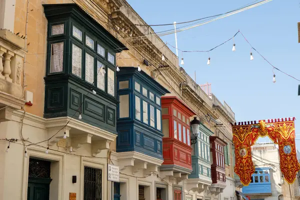 Rabat, Malta - 8 Ekim 2023: Geleneksel Malta 'nın kapalı balkonlarından oluşan canlı bir sıra, Rabat' ta tarihi bir cadde, şenlikli ışıklar ve afişlerle süslenmiş..