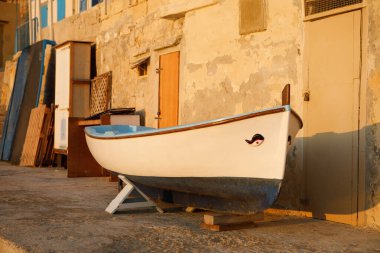 Geleneksel bir Malta balıkçı teknesi, 'luzzu' olarak da bilinir, Valletta, Malta 'da altın saat boyunca yıpranmış binaların yakınında duruyor.