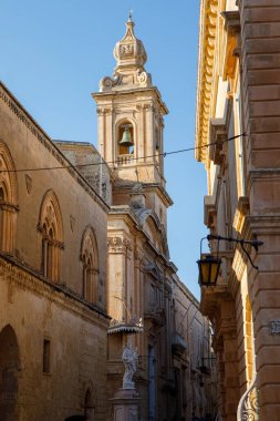 Aziz Paul Katedrali 'nin süslü çan kulesi tarihi bir Mdina caddesinin üzerinde yükselir ve Malta' da bir heykel ve geleneksel binalar bulunur.