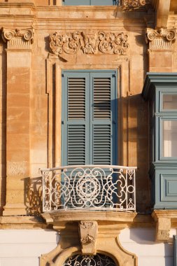Malta 'nın Valletta kentinde barok tarzı bir taş binayı süsleyen beyaz süslemeli ve mavi panjurlu geleneksel bir Malta balkonu var.