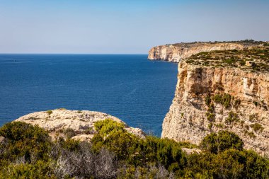 Akdeniz 'in berrak mavi ve turkuaz sularına, Birzebbuga, Malta' da parlak bir gökyüzü altında dramatik kireçtaşı kayalıkları düşüyor.