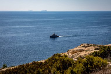 Küçük bir tekne, Birzebbuga, Malta 'daki kayalık ve bitkisel bir sahil şeridinden gözlemlenen, derin mavi Akdeniz' in geniş genişliğinde yol alır.