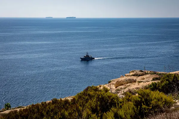 Küçük bir tekne, Birzebbuga, Malta 'daki kayalık ve bitkisel bir sahil şeridinden gözlemlenen, derin mavi Akdeniz' in geniş genişliğinde yol alır.