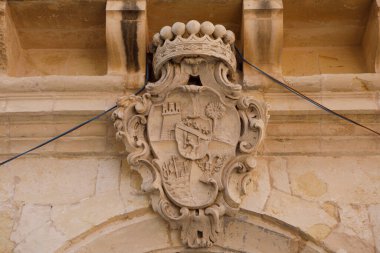 Süslü taş bir kalkan, bir kale ve palmiye ağacıyla habercilik, Rabat, Malta 'da eski bir bina cephesi süsleyen