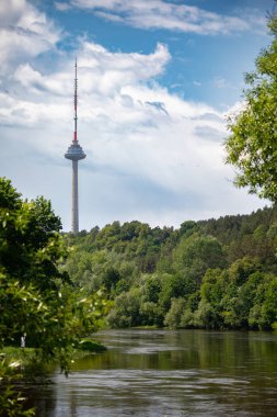 İkonik Vilnius TV Kulesi, dinamik bir gökyüzünün altında sakin Neris Nehri 'nin aktığı Vingis Park' ın yemyeşil ormanının üzerinde duruyor.