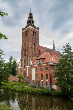 Lidzbark Warminski 'nin büyük kırmızı tuğlalı kilise kulesi, yeşil ağaçlar ve Polonya' nın bitişiğindeki binalarla çevrili sakin nehirde yansımasıyla ufuk çizgisine hükmediyor.