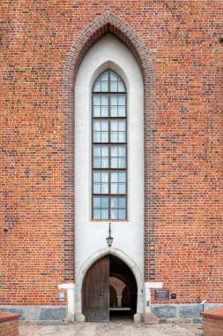 Lidzbark Warminski Kalesi 'nin etkileyici müze girişi. Polonya' da kırmızı tuğlalı bir cephede açık ahşap bir kapının üzerinde uzun kemerli bir pencere var.