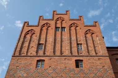 Polonya 'nın Olsztyn kentindeki tarihi Yukarı Kapı' nın süslü merdivenlerinde mavi gökyüzüne karşı karmaşık kırmızı tuğlalar ve kemerli pencereler yer alıyor.