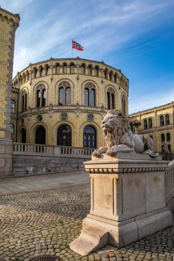 Oslo, Norveç - 15 Temmuz 2025: İkonik Stortinget Parlamentosu binası Norveç bayrağı altında ana girişi koruyan taş bir aslan heykeli ile gururla duruyor.