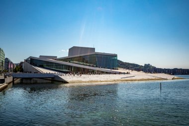 Oslo, Norveç - 18 Temmuz 2025: Oslo Opera Binası 'nın çarpıcı beyaz mermer ve cam mimarisi fiyorda insanların erişilebilir çatı ve güneşli deniz manzarasının keyfini çıkardığı yamaçlara sahiptir..