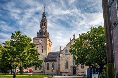 Oslo, Norveç - 15 Temmuz 2025: Tarihi Oslo Domkirke (Oslo Katedrali), kendine özgü saat kulesiyle, canlı bir gökyüzünün altındaki yeşil ağaçların arasında duruyor..