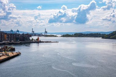Oslo, Norveç - 15 Temmuz 2025: Uzak kıyılarda sanayi turnaları, yeşil adalar ve dinamik bir gökyüzü altında şehrin deniz sanayi manzarasını vurgulayan uçsuz bucaksız genişlikte su içeren geniş Oslo Fiyortu.