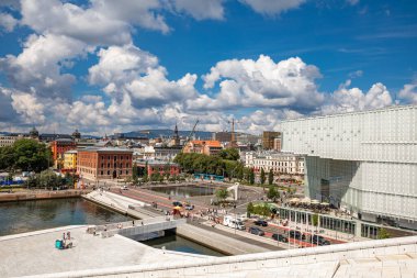 Oslo, Norveç - 15 Temmuz 2025: Opera Binası 'nın eşsiz mimarisi, hareketli bir liman ve canlı bir gökyüzü altında tarihi ve modern binaların karışımının yer aldığı Oslo şehir merkezinin panoramik görüntüsü.
