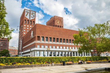 Oslo, Norveç - 15 Temmuz 2025: Oslo Belediye Binası 'nın ikonik tuğla kuleleri, ön planda yemyeşil bir bahçesi ve bankları olan bir yaz gökyüzüne karşı duruyor..