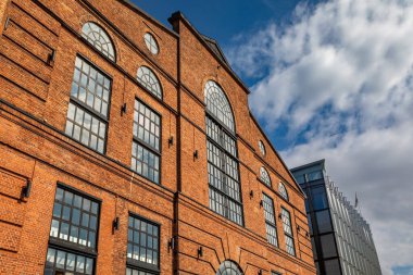 Tarihi bir kırmızı tuğla bina, Aker Brygge 'ın yenilenmiş liman bölgesindeki modern cam cephenin yanında duruyor.