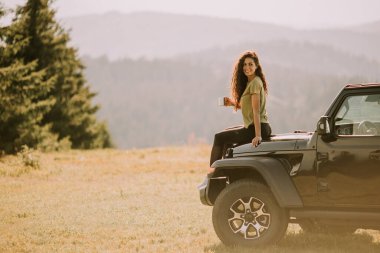 Pretty young woman relaxing on a terrain vehicle hood at countryside