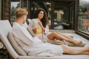 Yakışıklı genç çift yataklarında dinleniyor ve terasta taze portakal suyu içiyor.