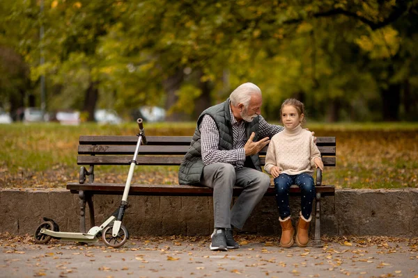 秋の日に孫と一緒に公園のベンチで過ごすハンサムな祖父 — ストック写真