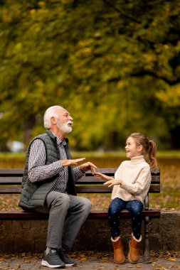 Yakışıklı büyükbaba, sonbahar günü torunuyla parkta el pençe oyunu oynuyor.