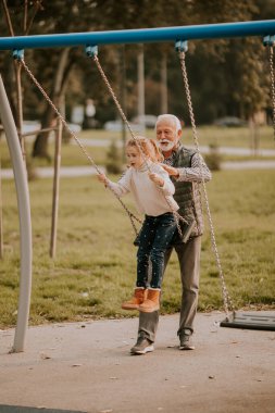 Yakışıklı büyükbaba, sonbahar günü torunuyla parkta vakit geçiriyor.