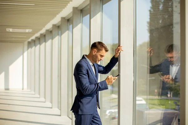 現代のオフィスの廊下で携帯電話を使用してハンサムな若いビジネスマン — ストック写真