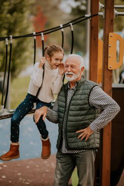 Yakışıklı büyükbaba, sonbahar günü torunuyla parkta vakit geçiriyor.